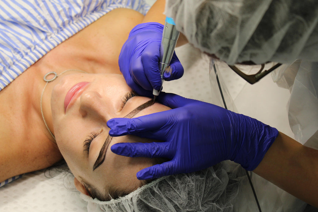 Eyebrow Cosmetic Tattoo in progress with THink Aesthetics technician holding a cosmetic tattoo machine, half way through tattooing a client's brows