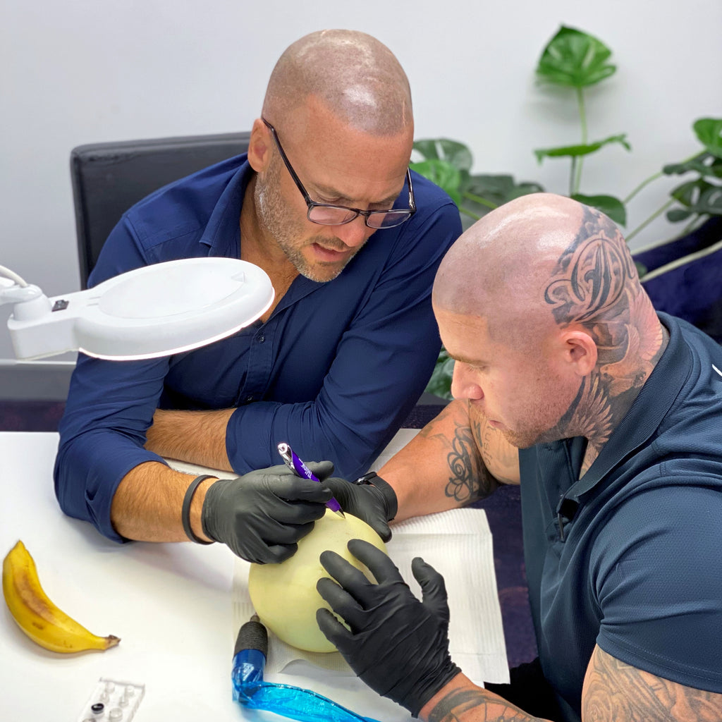 Mike Gunner training Scalp Micropigmentation for THink Aesthetics, assisting student learning Scalp Micropigmentation by showing him on a rockmelon